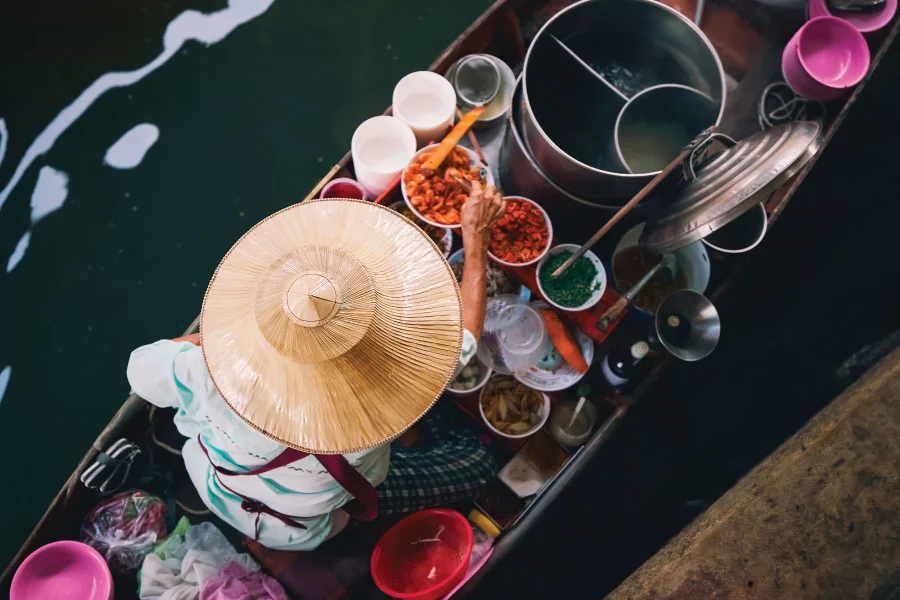 a person wearing a traditional hat selling foods on a wooden boat floating on water