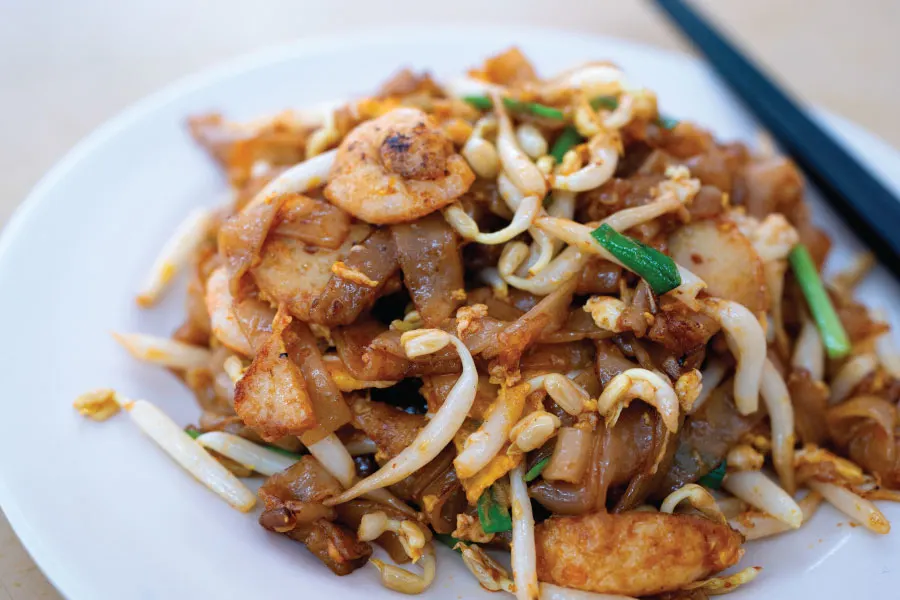 fried flat rice noodles with chives, beansprouts, prawns and cockles served on a white plate