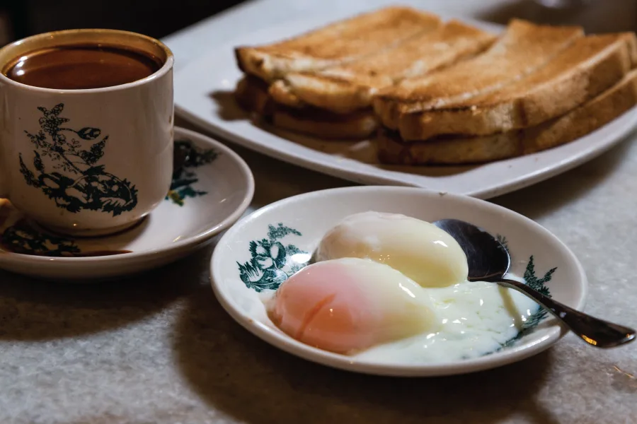 coffee with milk served on a traditional cup, half boiled eggs and toast